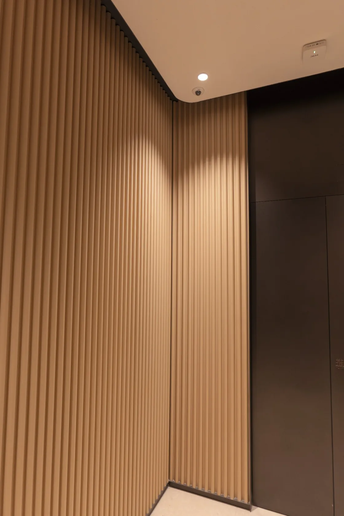 Vertical terracotta ribs wrapping an EIC interior corner next to a dark wall panel.