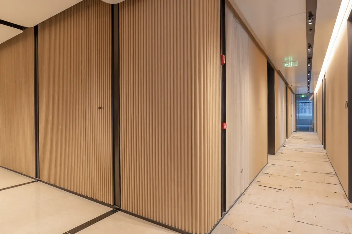 EIC corridor junction with tall vertical terracotta ribs, dark trims and temporary floor protection.